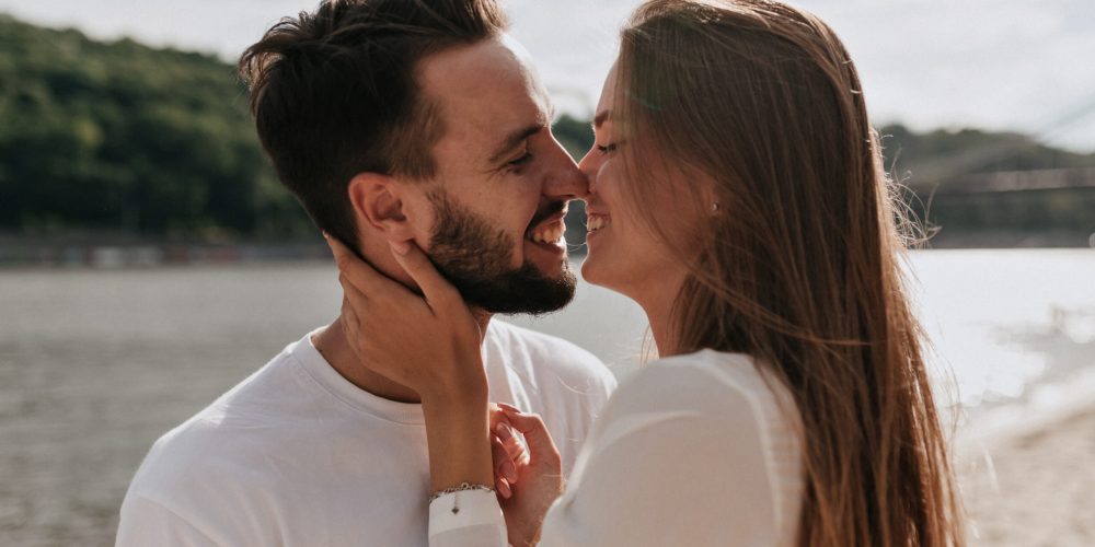 feliz-pareja-enamorados-abrazandose-besandose-juntos-playa-calido-dia-soleado